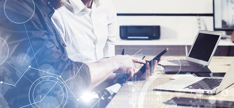 Concept of digital screen,virtual connection icon,diagram,graph interfaces.Bearded young man holding mobile phone and touching display.Adult businessman working together with partner.Film effect,wide.